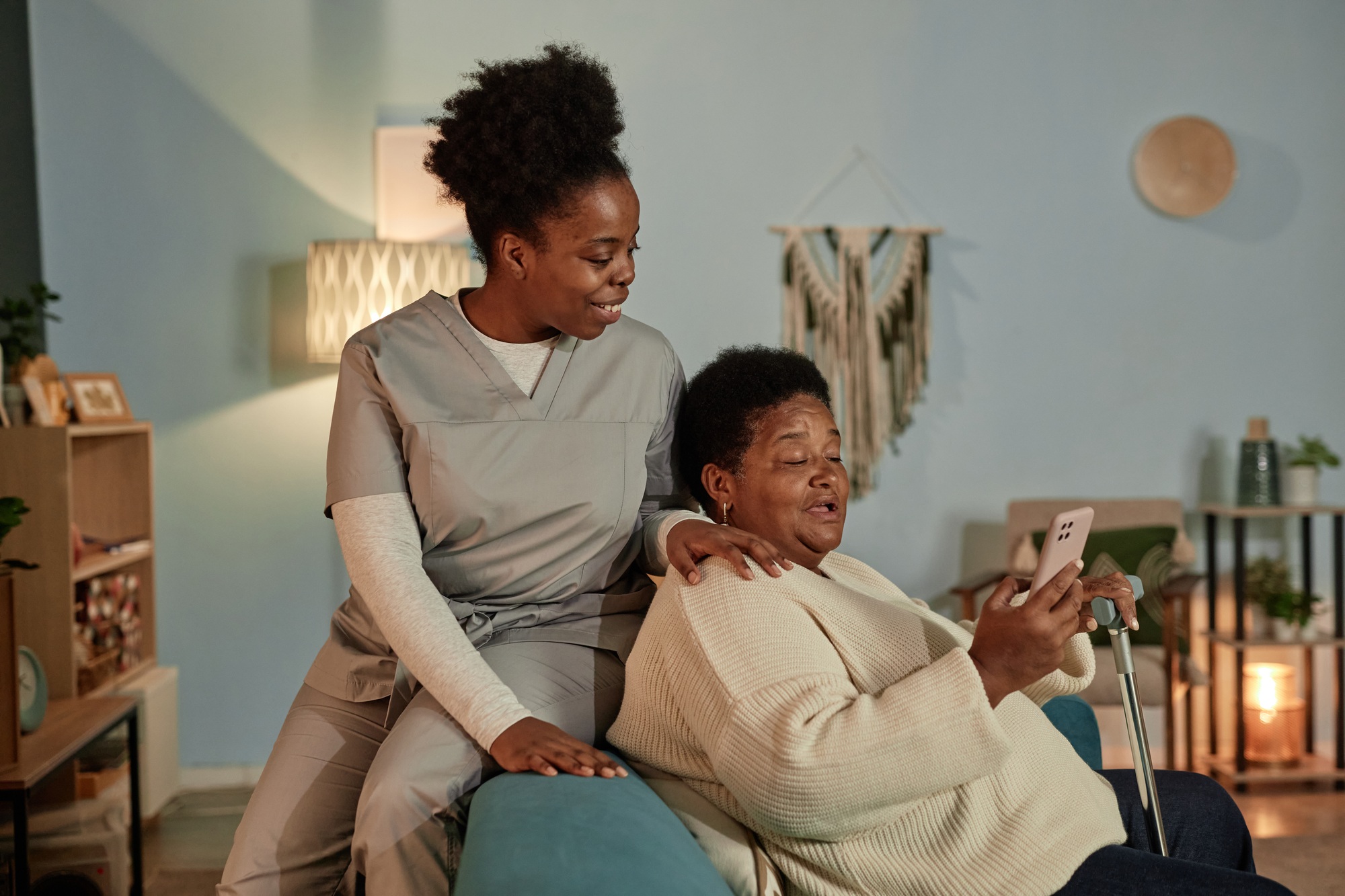 Elderly Woman Using Smartphone with Smiling Caregiver at Home