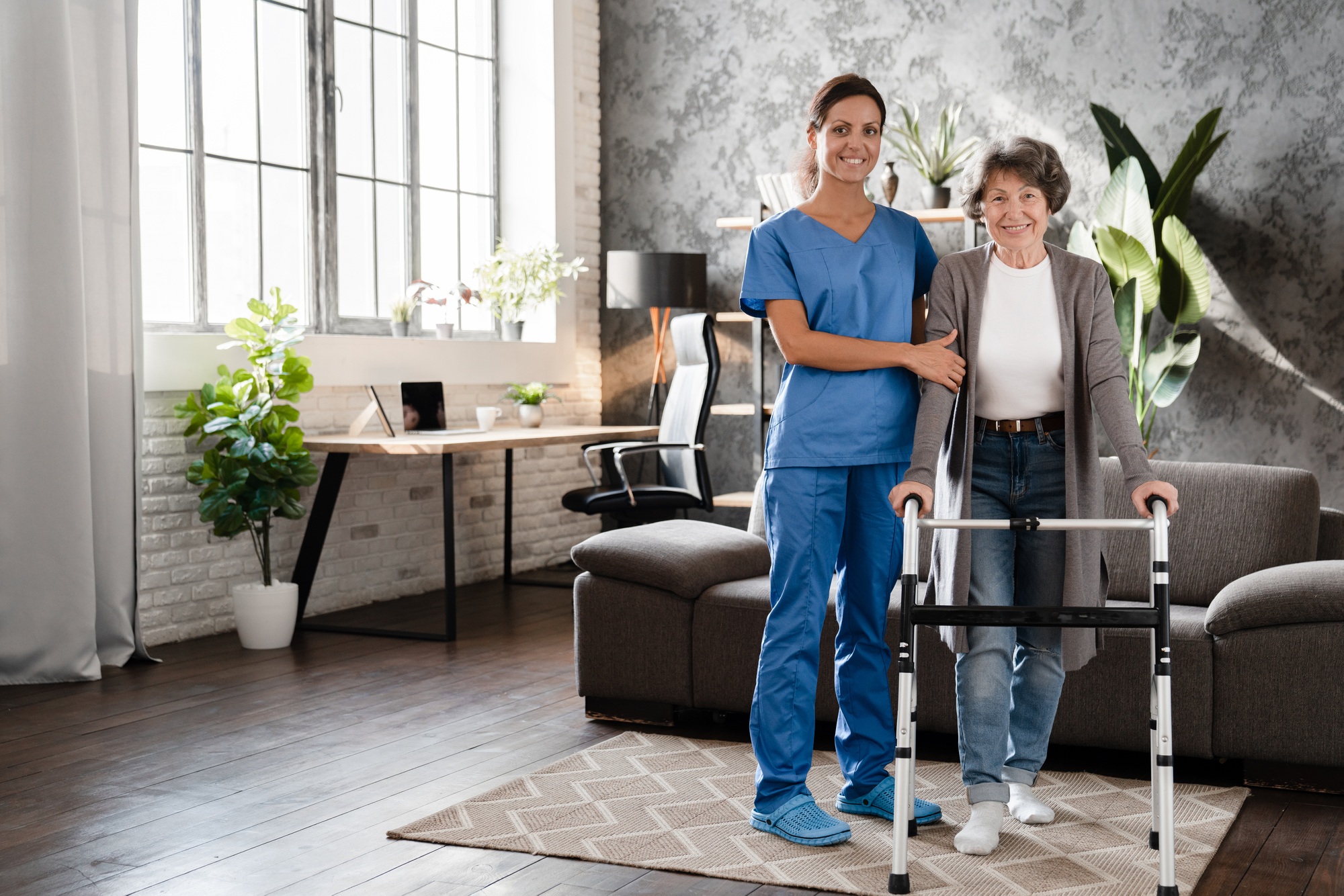 Happy pensioner grandmother patient with walking frame with assistance of nurse caregiver at home